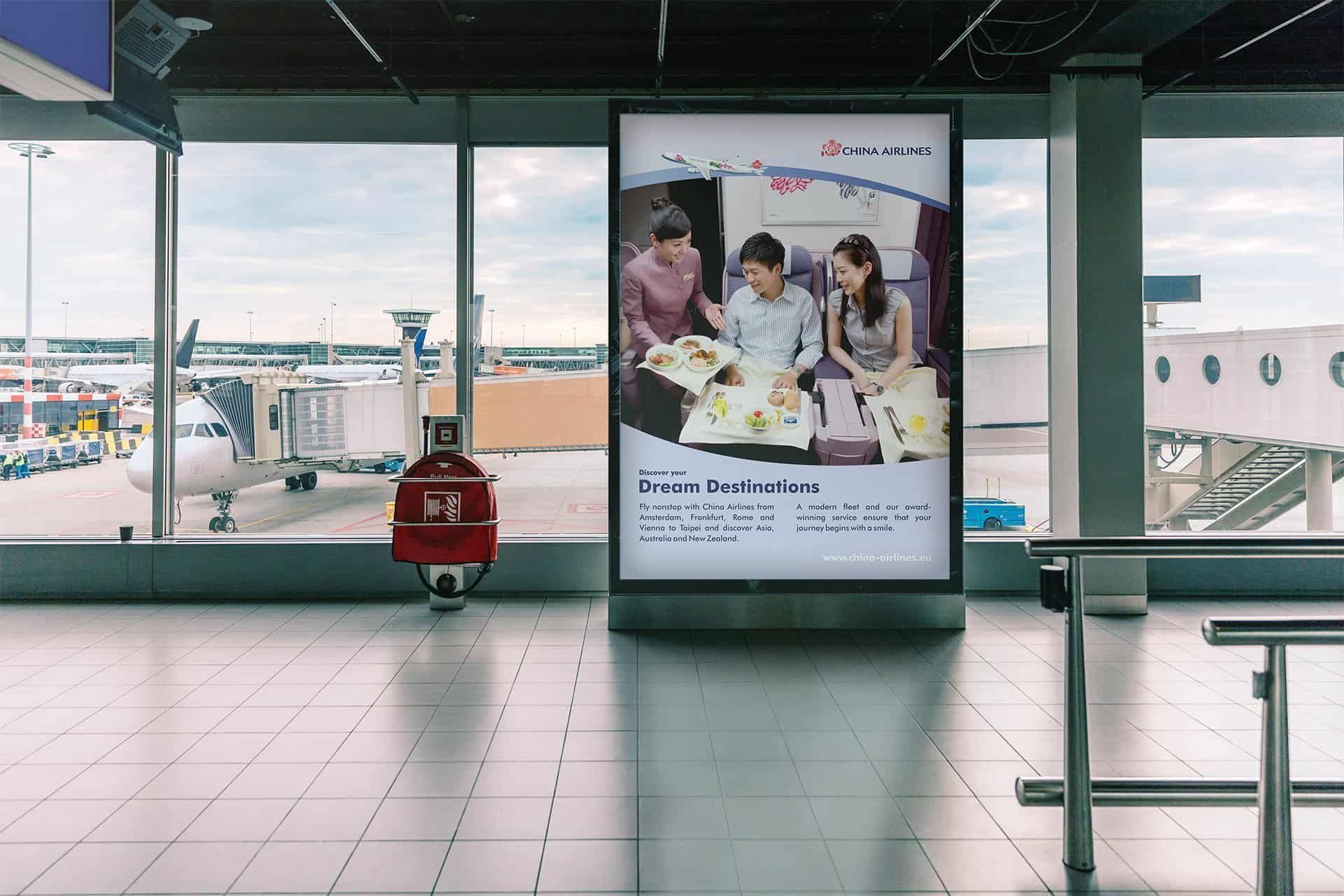 City light poster at an airport in front of a window onto the apron: a flight attendant serving a meal to two passengers, with the title “Dream Destinations”