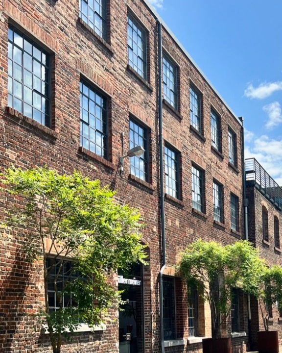 Brick façade of the Heyne Fabrik with steel-framed windows and trees in planters