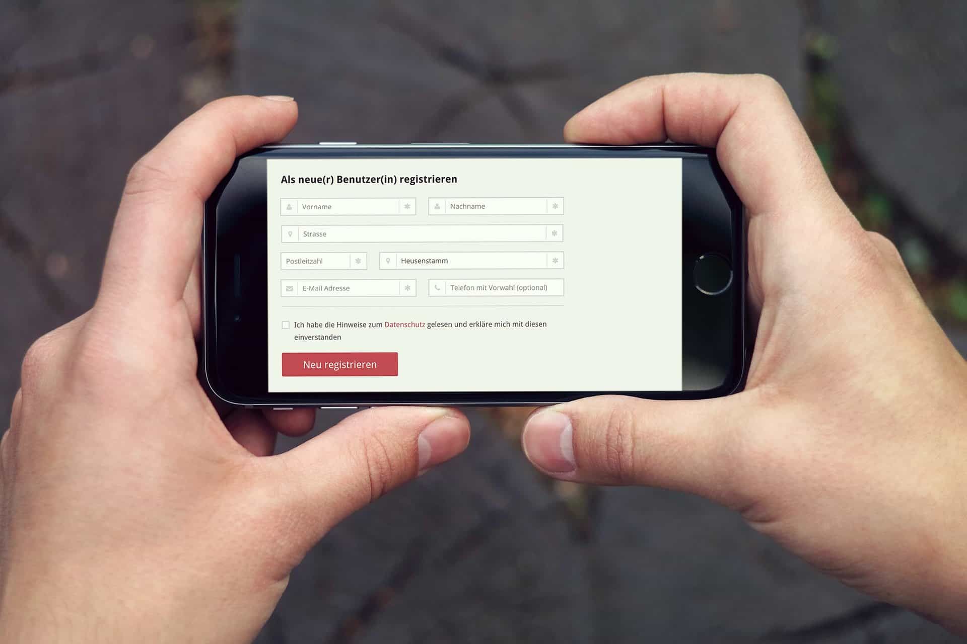 Two hands holding a smartphone sideways with the registration form for new users