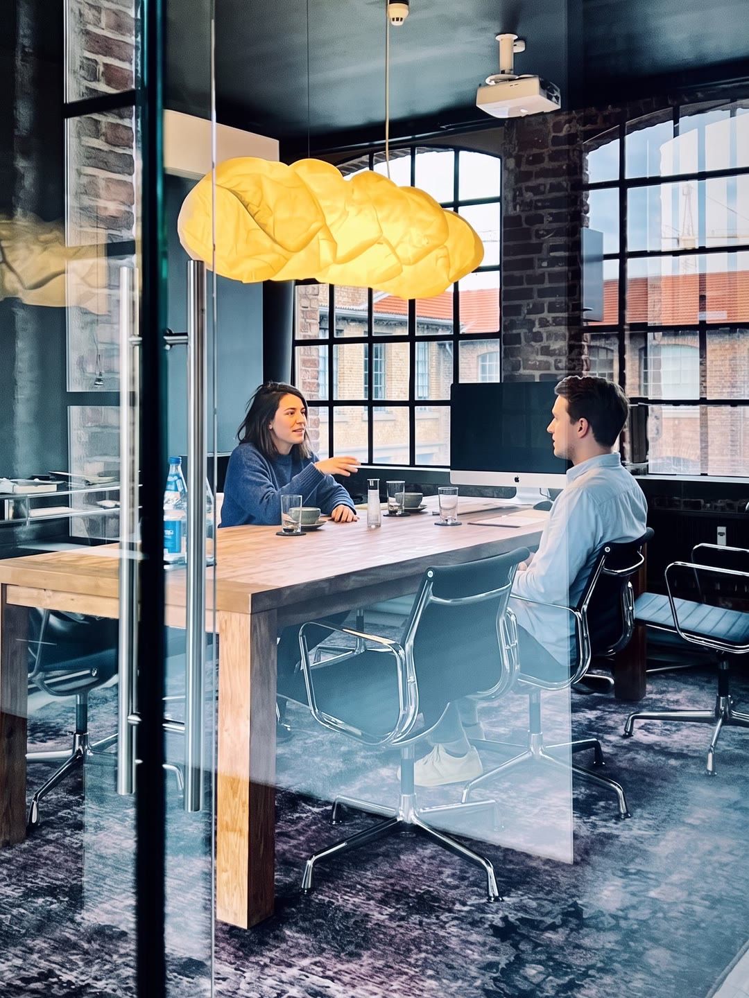 Two colleagues talking at the table of a glass-walled meeting room