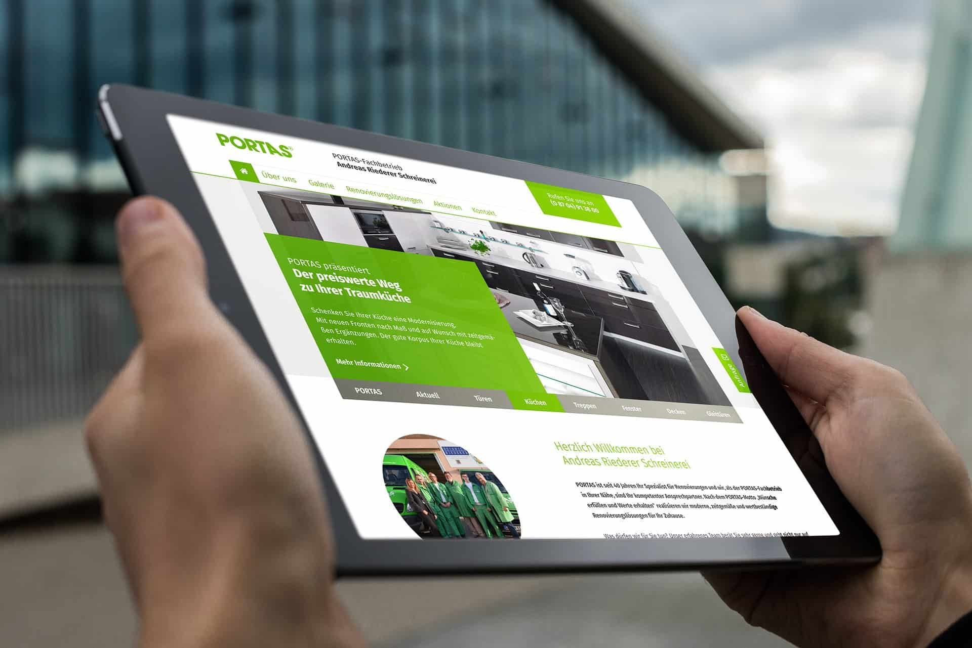 Hands holding a tablet with the website of a PORTAS franchise business, an office building with a glass facade behind