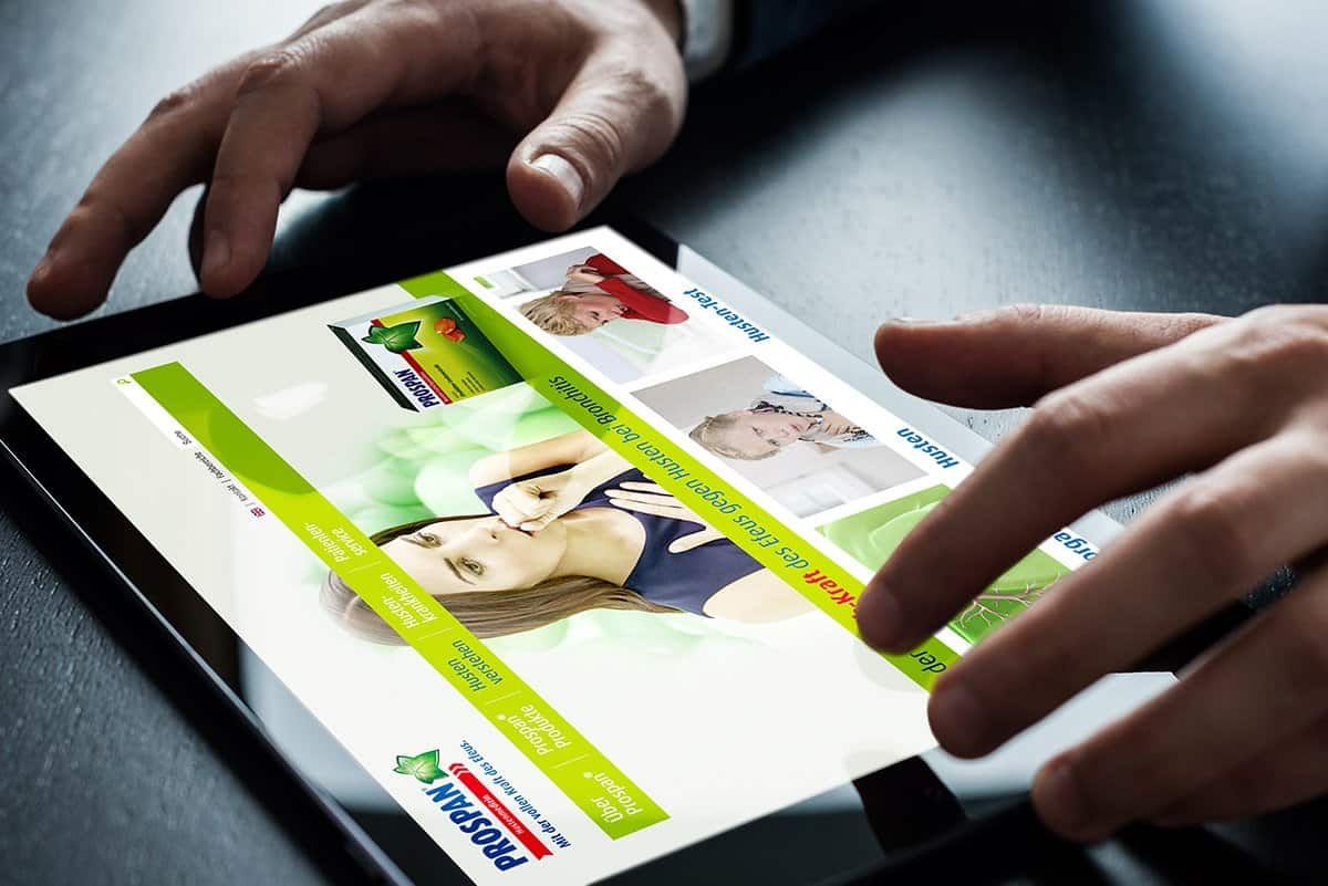 Hands over a tablet showing the Prospan website, with a pack of Prospan at the top and articles about coughs