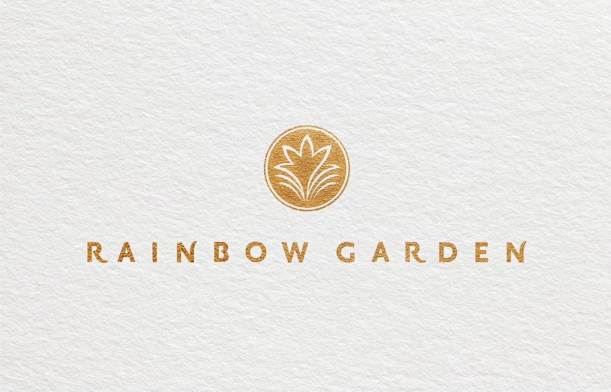Rainbow Garden logo foil-stamped in gold on textured white paper: flower mark in a circle and wordmark