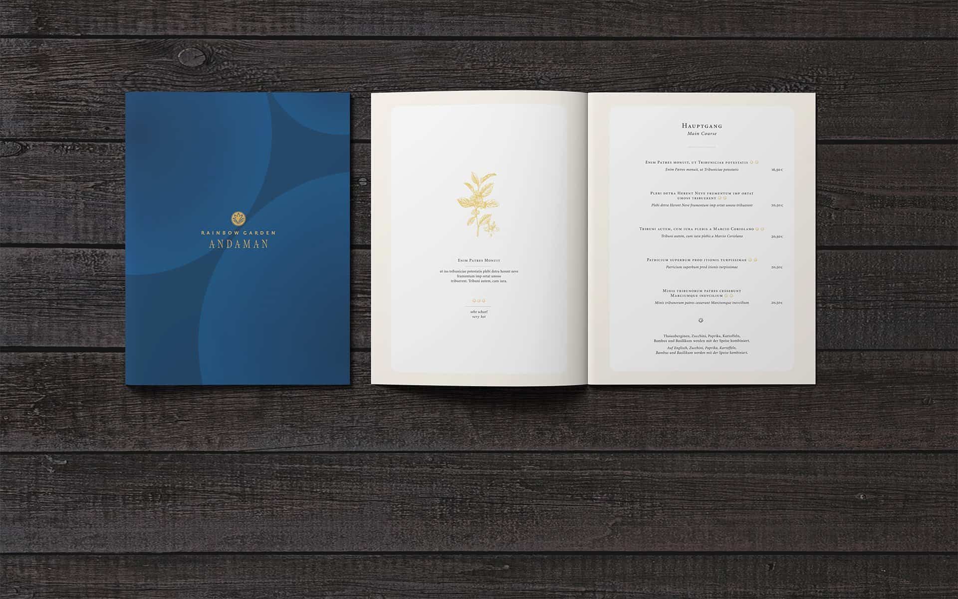 Rainbow Garden Andaman menu on a wooden table: blue cover with a gold logo, next to it the open pages with the main courses
