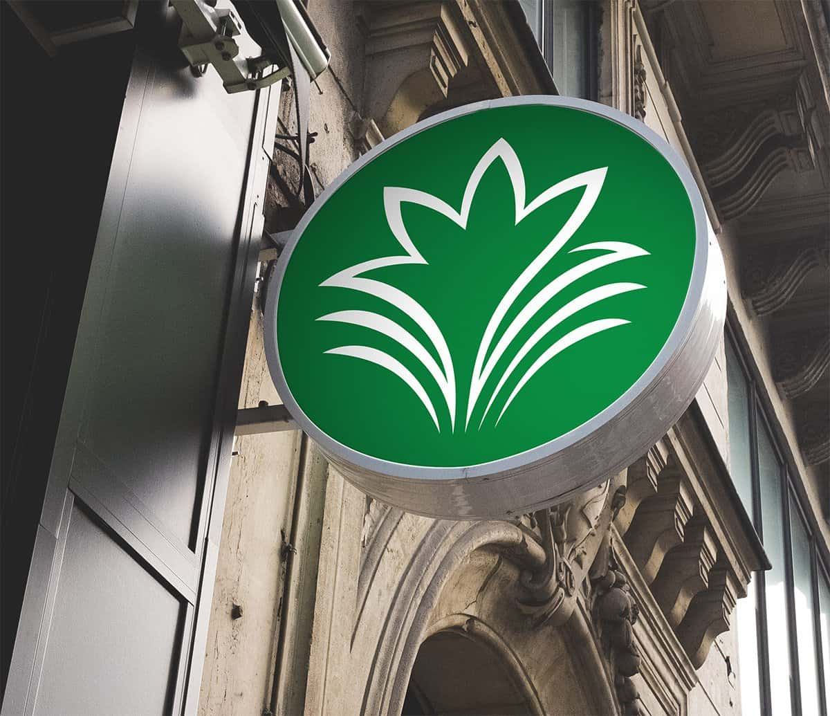 Round green illuminated sign with the white Rainbow Garden flower mark on the facade of an old building