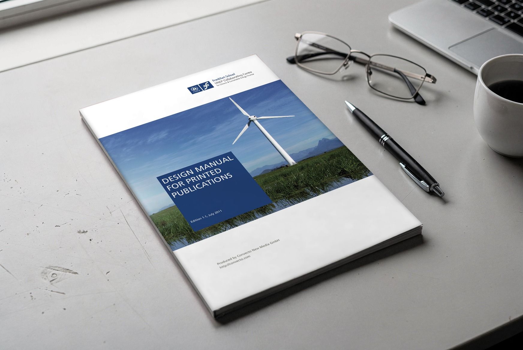 The printed design manual on a light desk, with glasses, a pen and a coffee cup beside it