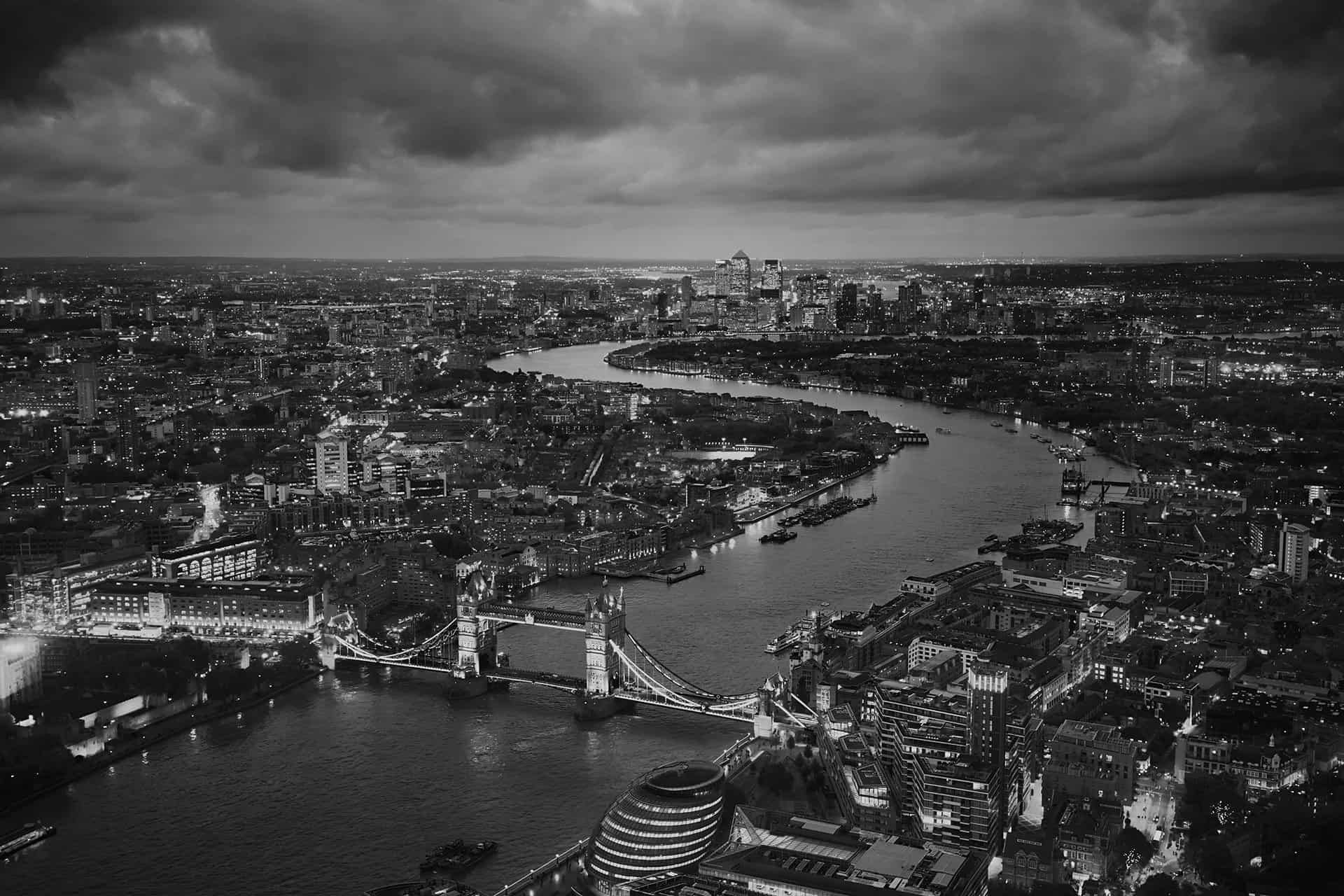 Black and white aerial view of London with Tower Bridge and the Thames, the towers of Canary Wharf on the horizon