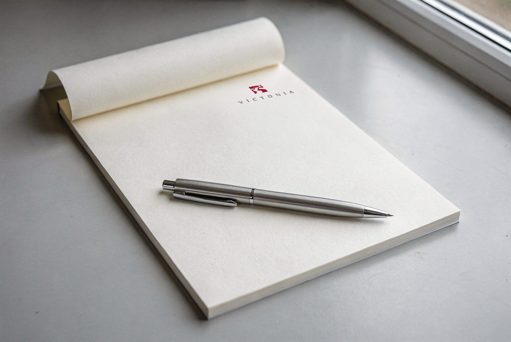 Notepad with the Victonia logo and a silver ballpoint pen
