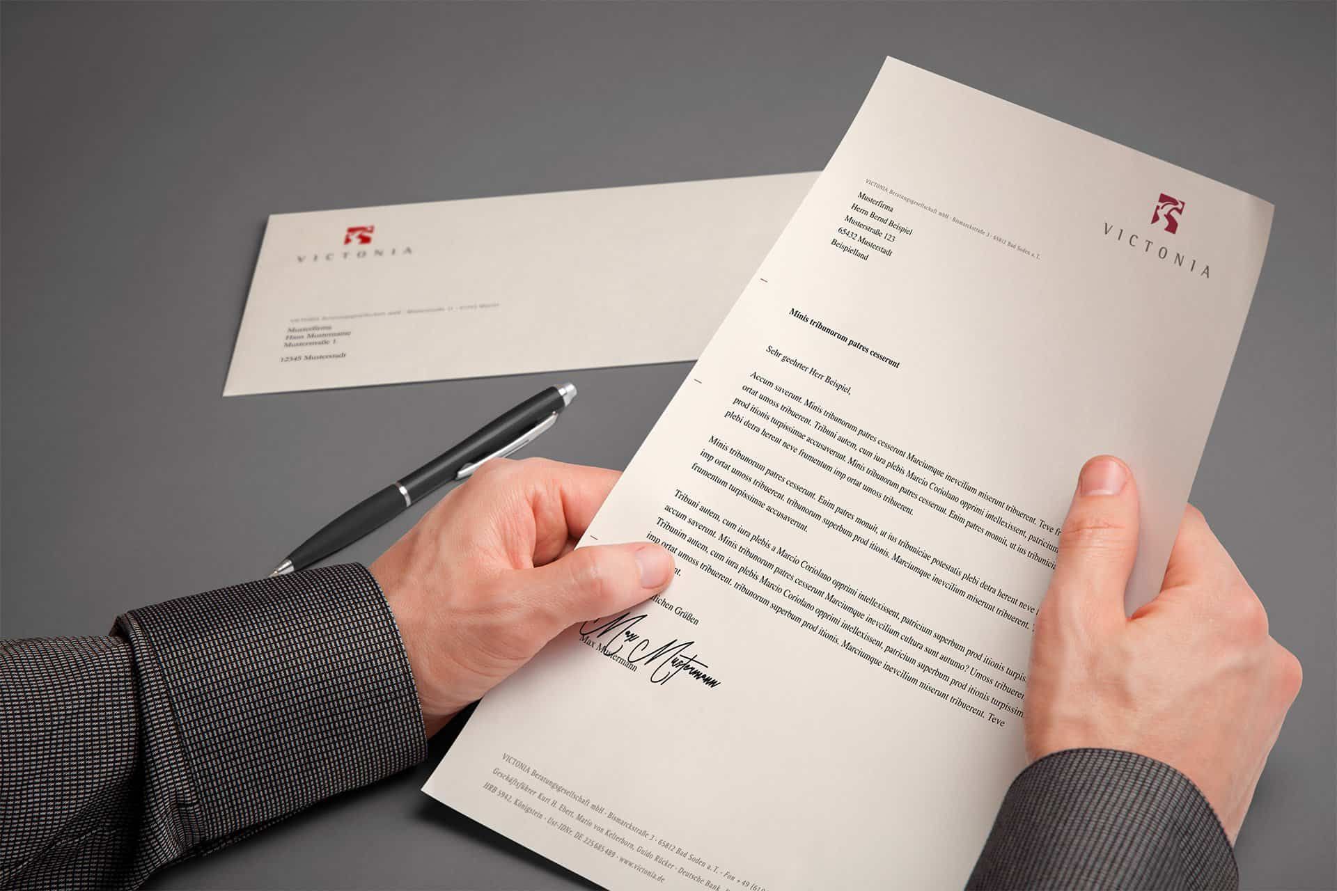 Hands holding a Victonia letterhead, with the envelope and a pen behind it