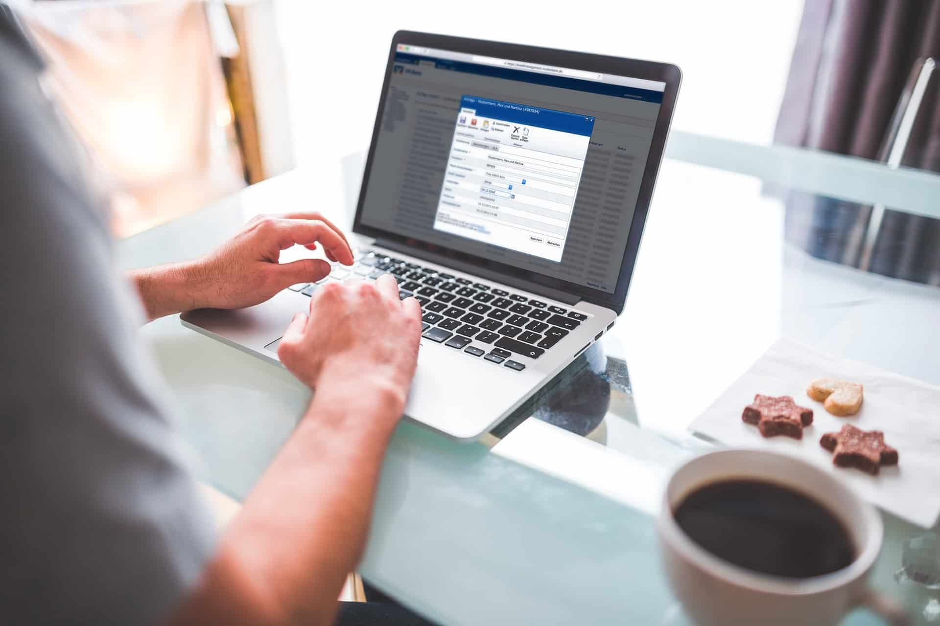 Person working on a loan application in the SLA compliance tool on a laptop, with coffee and biscuits beside it